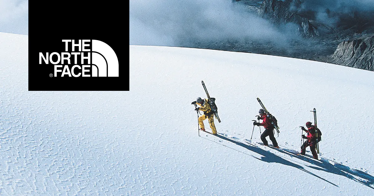 Three skiiers hike up a snowy mountain top