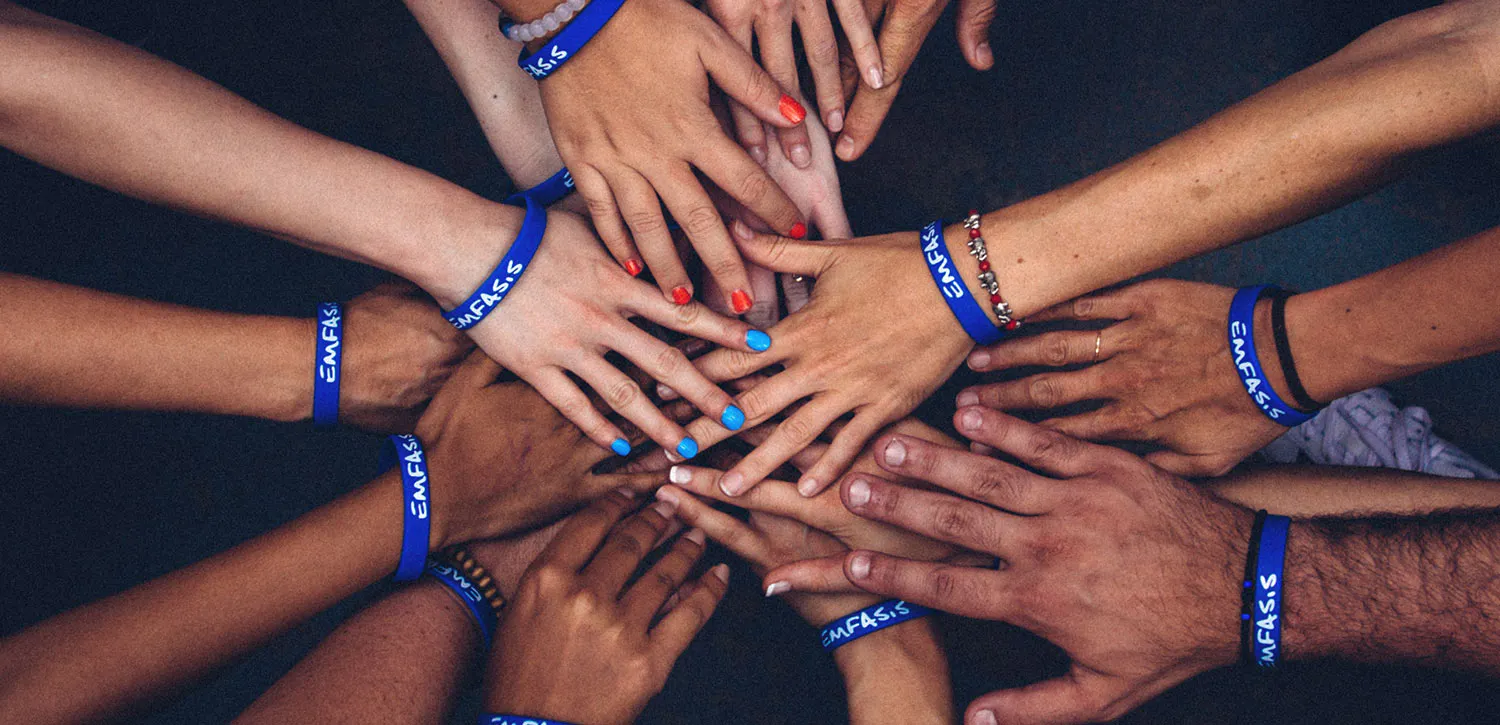 Closeup of diverse hands raised together each wearing brightly colored fundraising bracelets