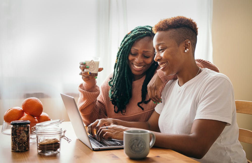 two women smiling drinking coffee and looking at a laptop computer