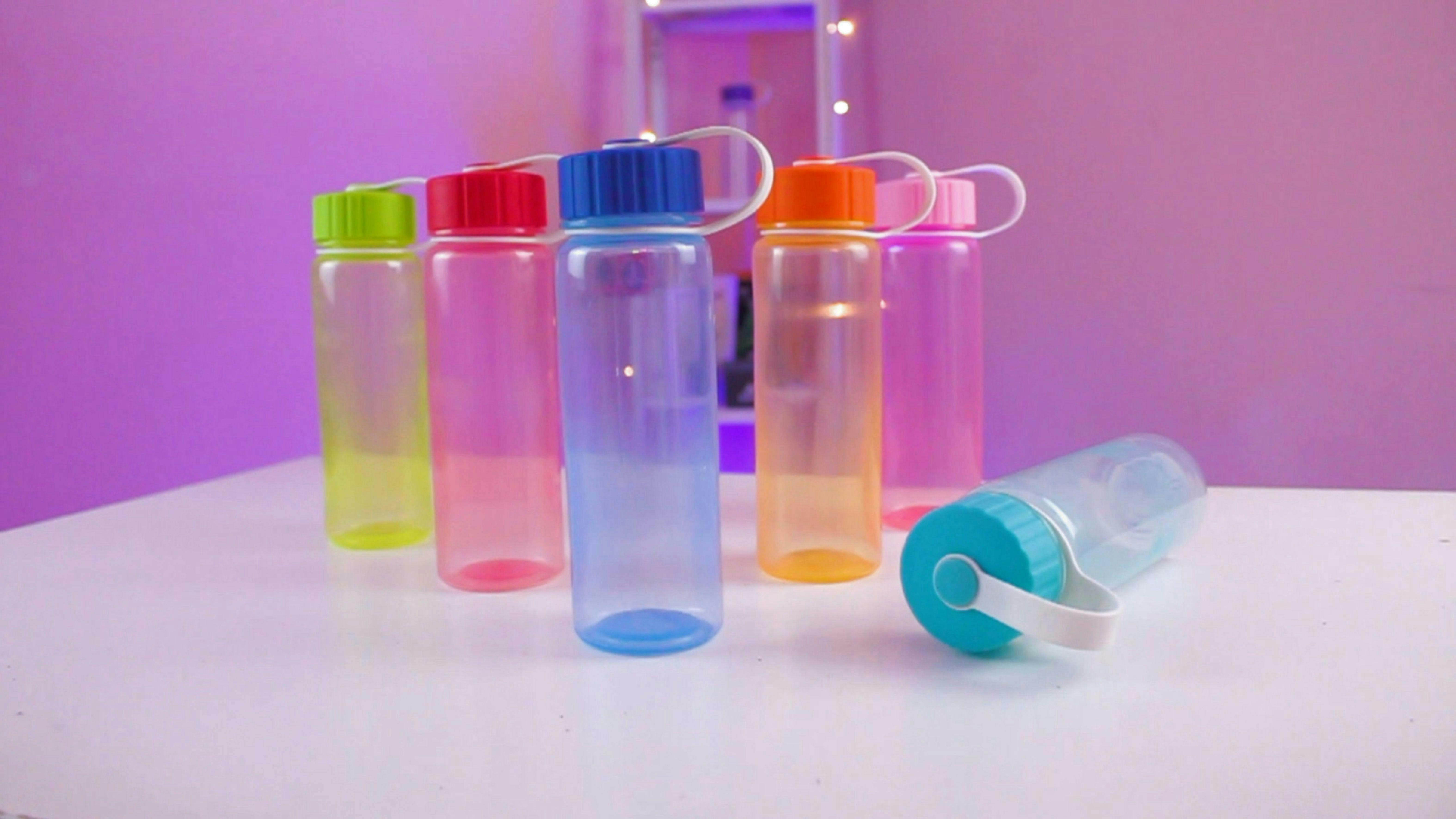 Six different color clear water bottles sitting on a table with one laying on its side