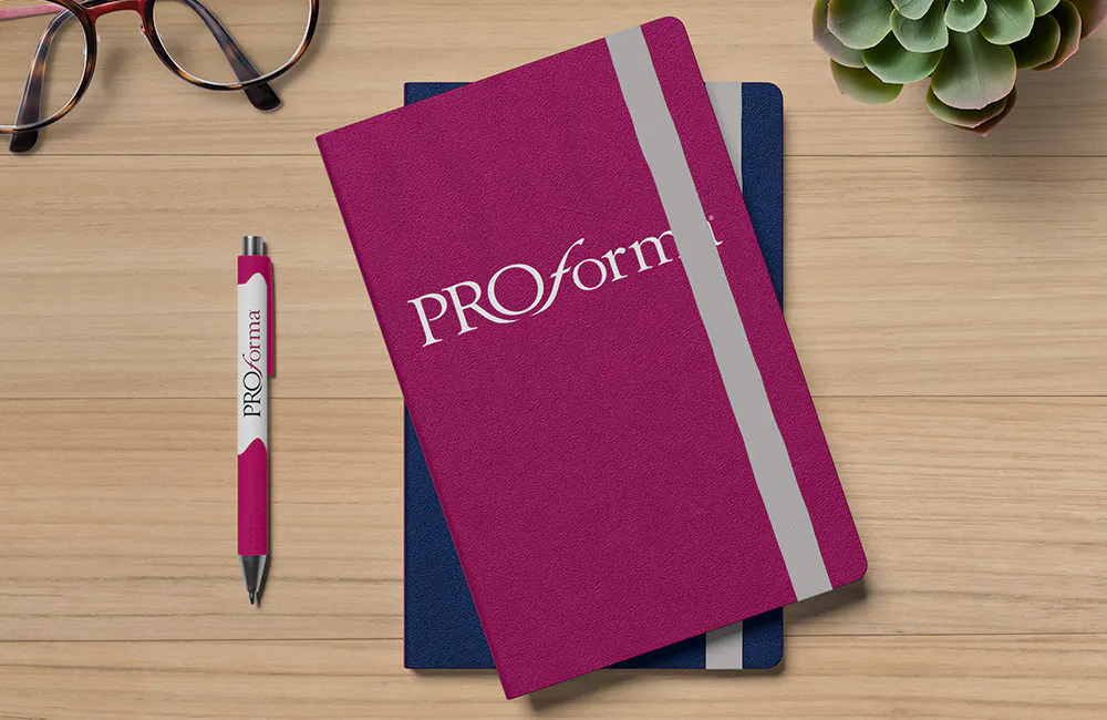 Proforma pink notebook with navy notebook underneath and Proforma branded pen next to it