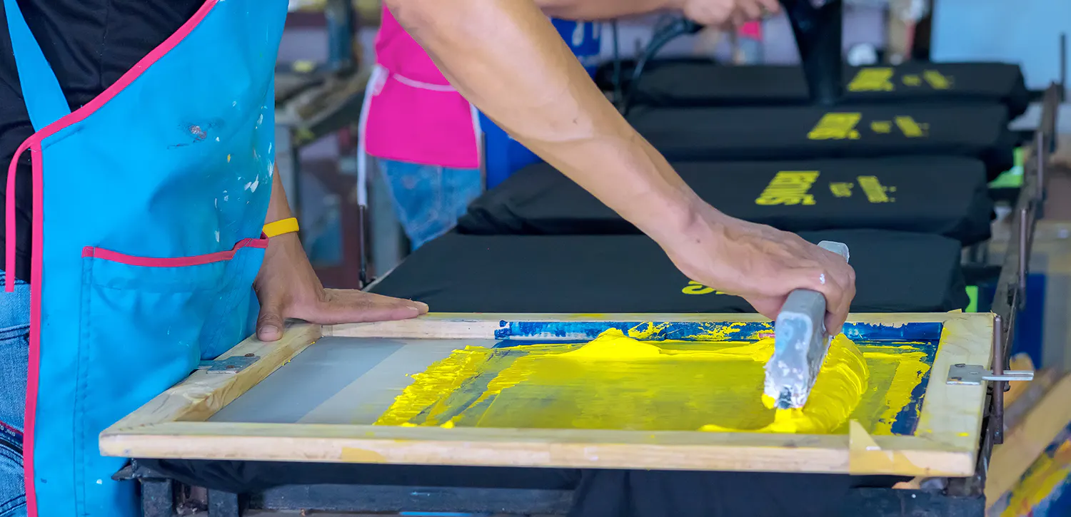 Man screen printing a t-shirt with yellow ink
