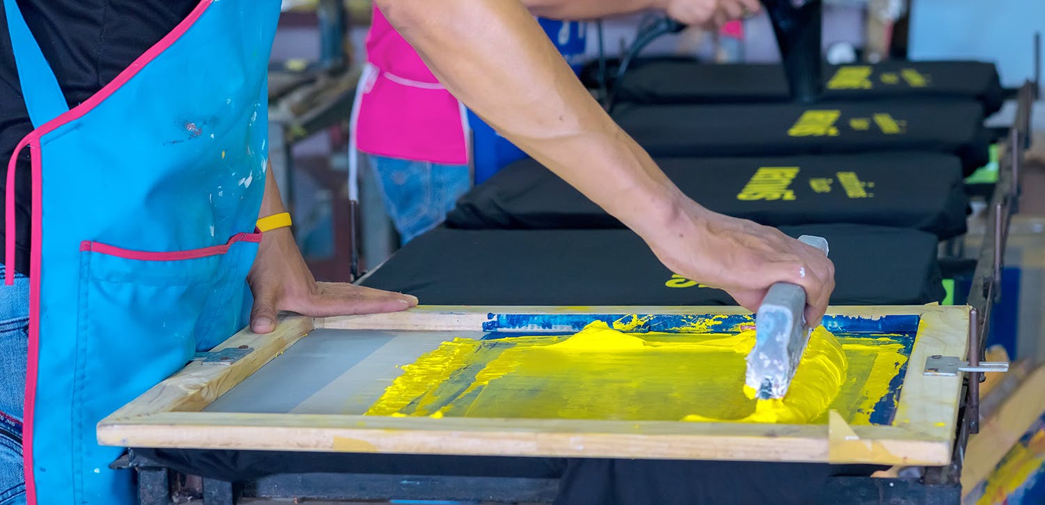 Man screen printing a t-shirt with yellow ink