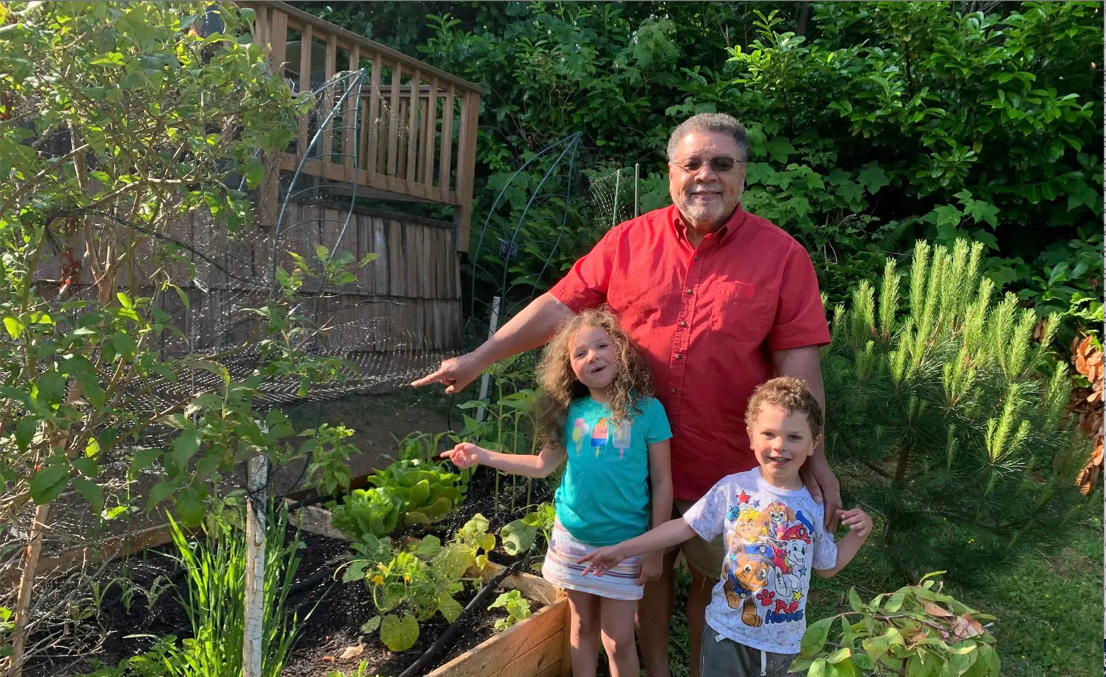 A man and two children pointing at their vegetable garden
