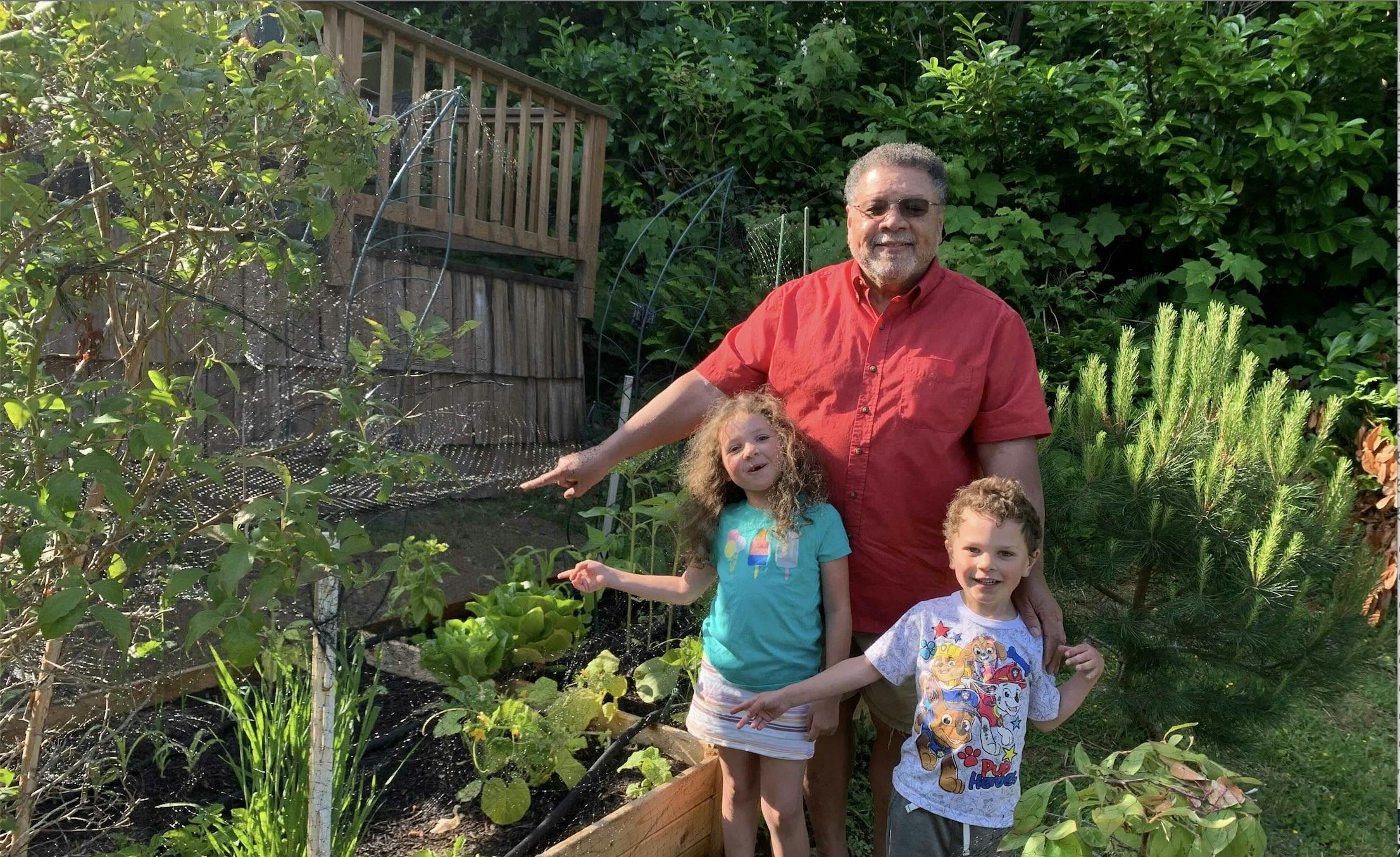 A man and two children pointing at their vegetable garden