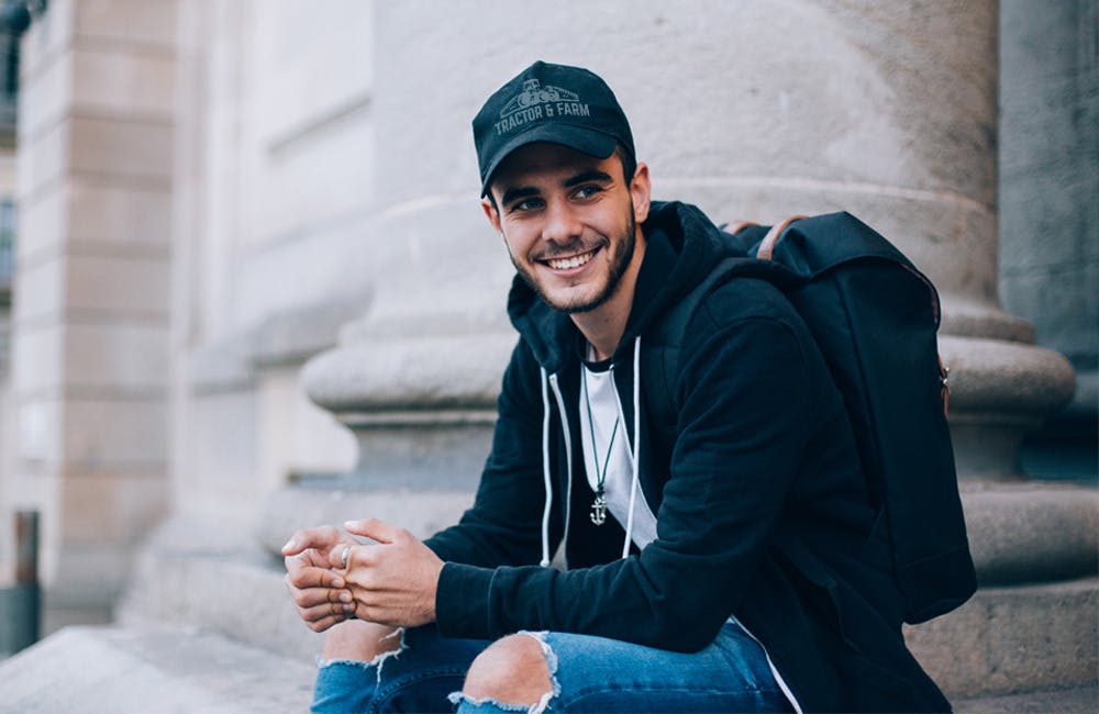 man smiling wearing logoed ball cap in an urban setting