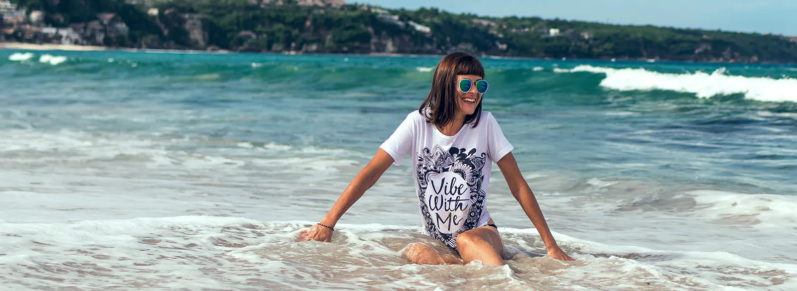 girl playfully wading in the water at the beach, wearing a white tshirt that says Vibe With Me