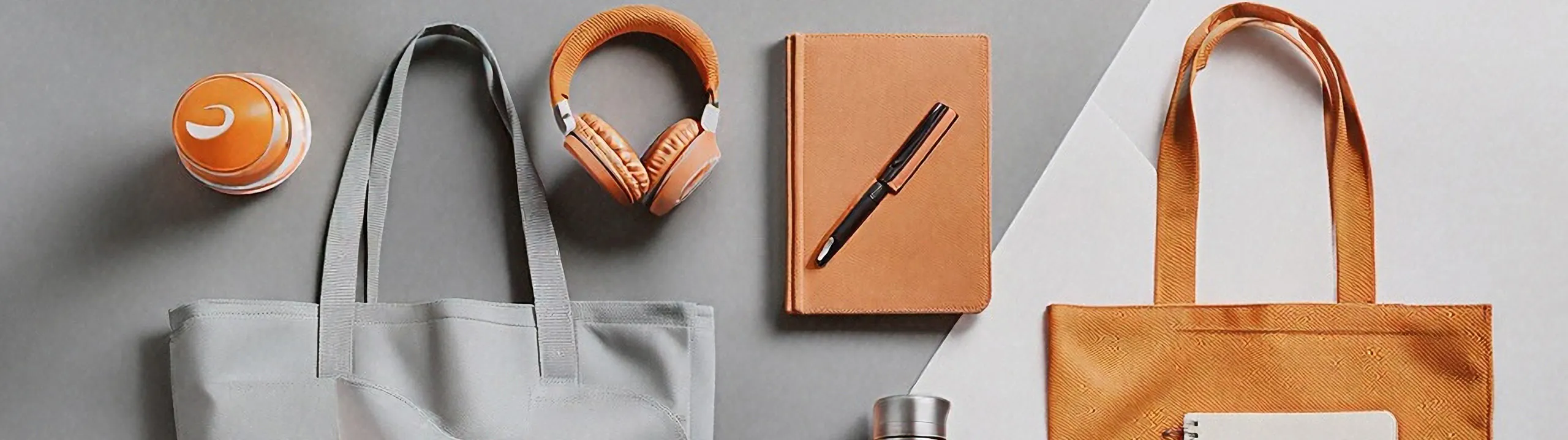 Collection of orange and gray items arranged neatly on the ground, including two tote bags, a notebook, and headphones