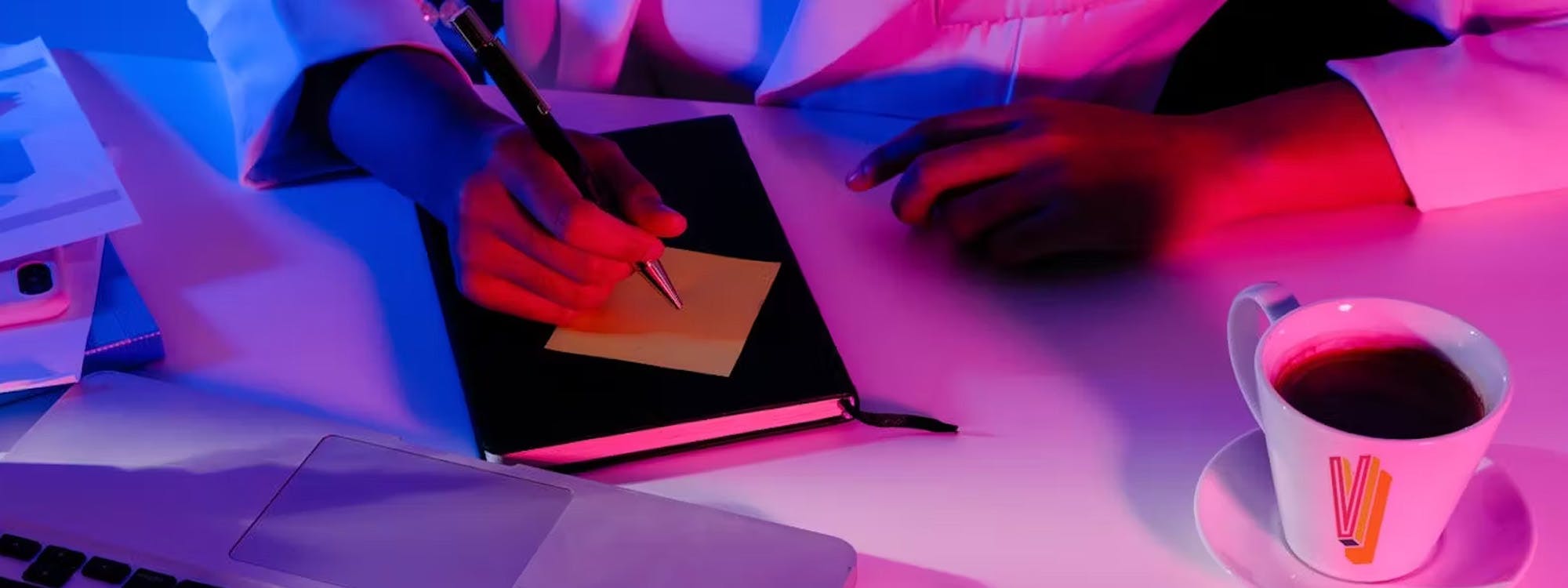overhead shot of a person writing in a notebook on a desk with a logoed coffee mug