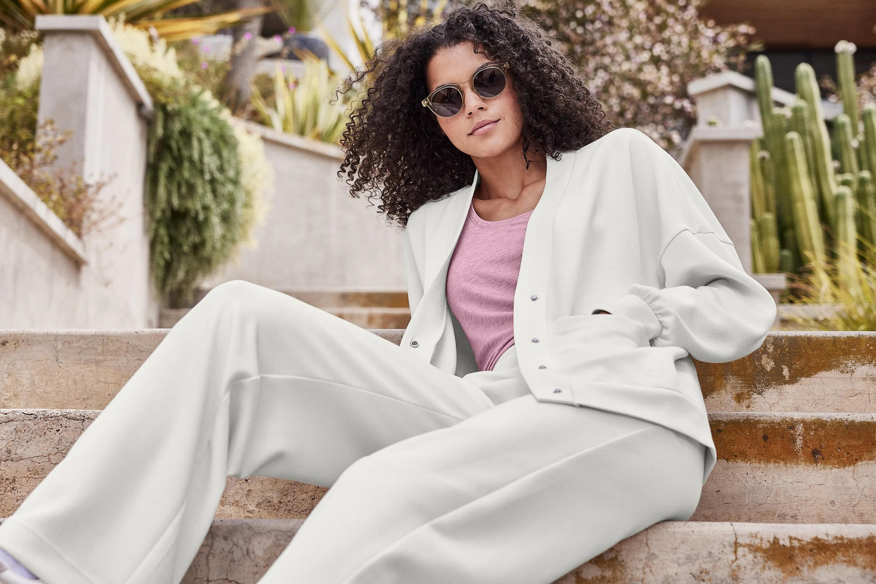 A woman in a snap cardigan and sleek pants poses on the stairs in a sunny location