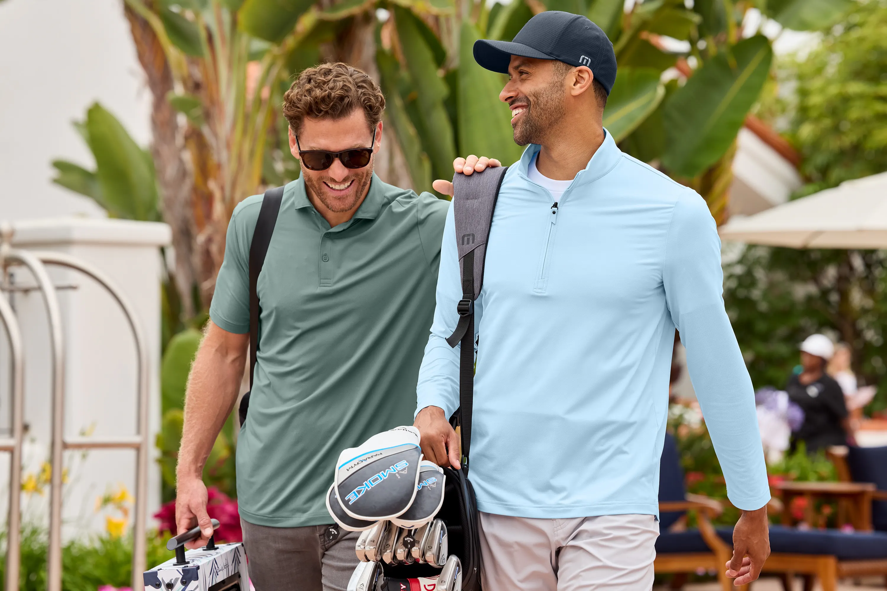 Two golfers wearing a lightweight quarter zip and a polo laugh as they walk away from their resort