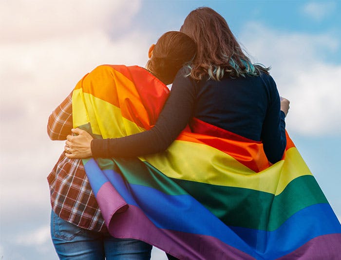 same sex couple hugging with pride flag wrapped around them