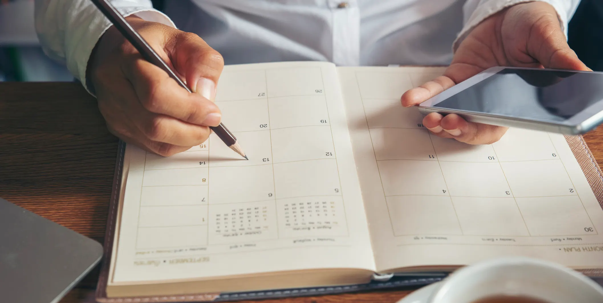 Man recording appts on phone and in planner at desk