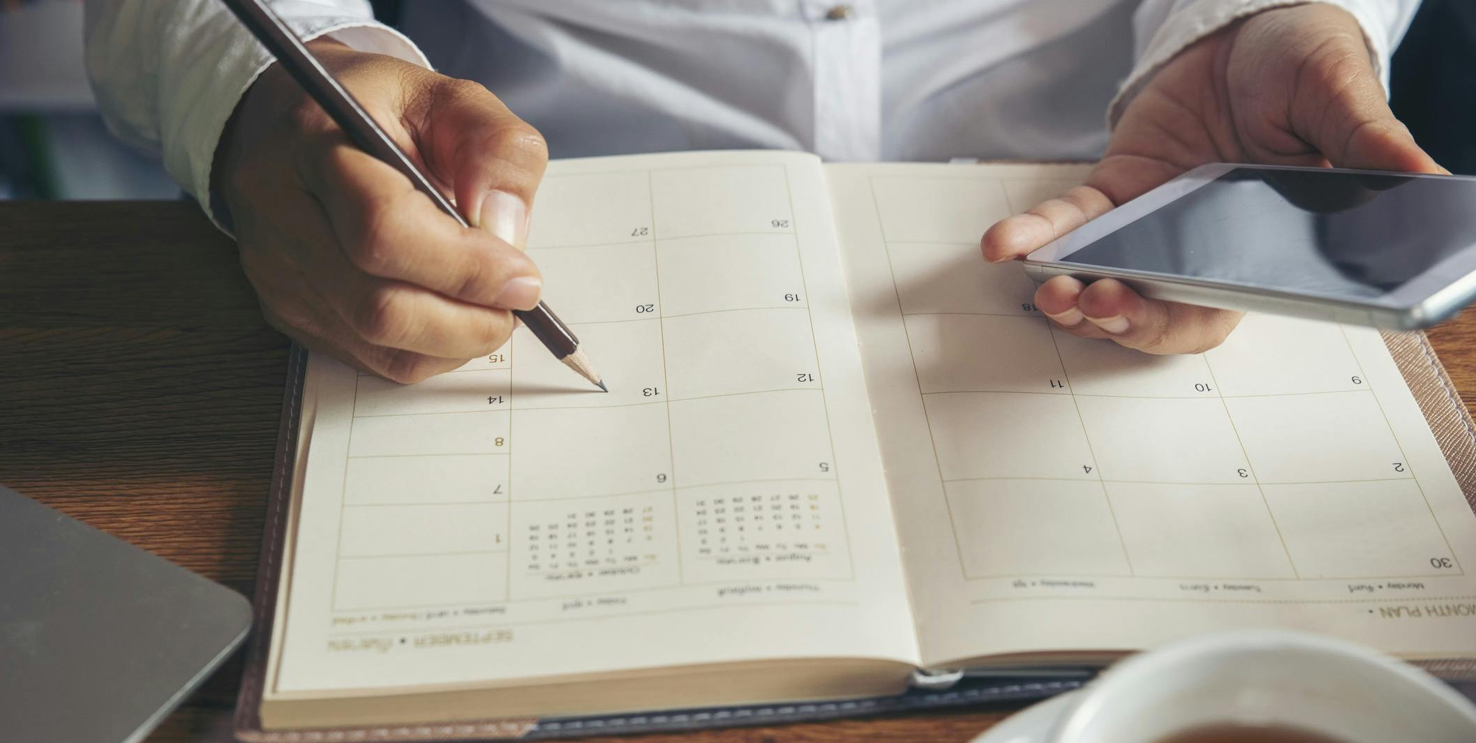 Man recording appts on phone and in planner at desk
