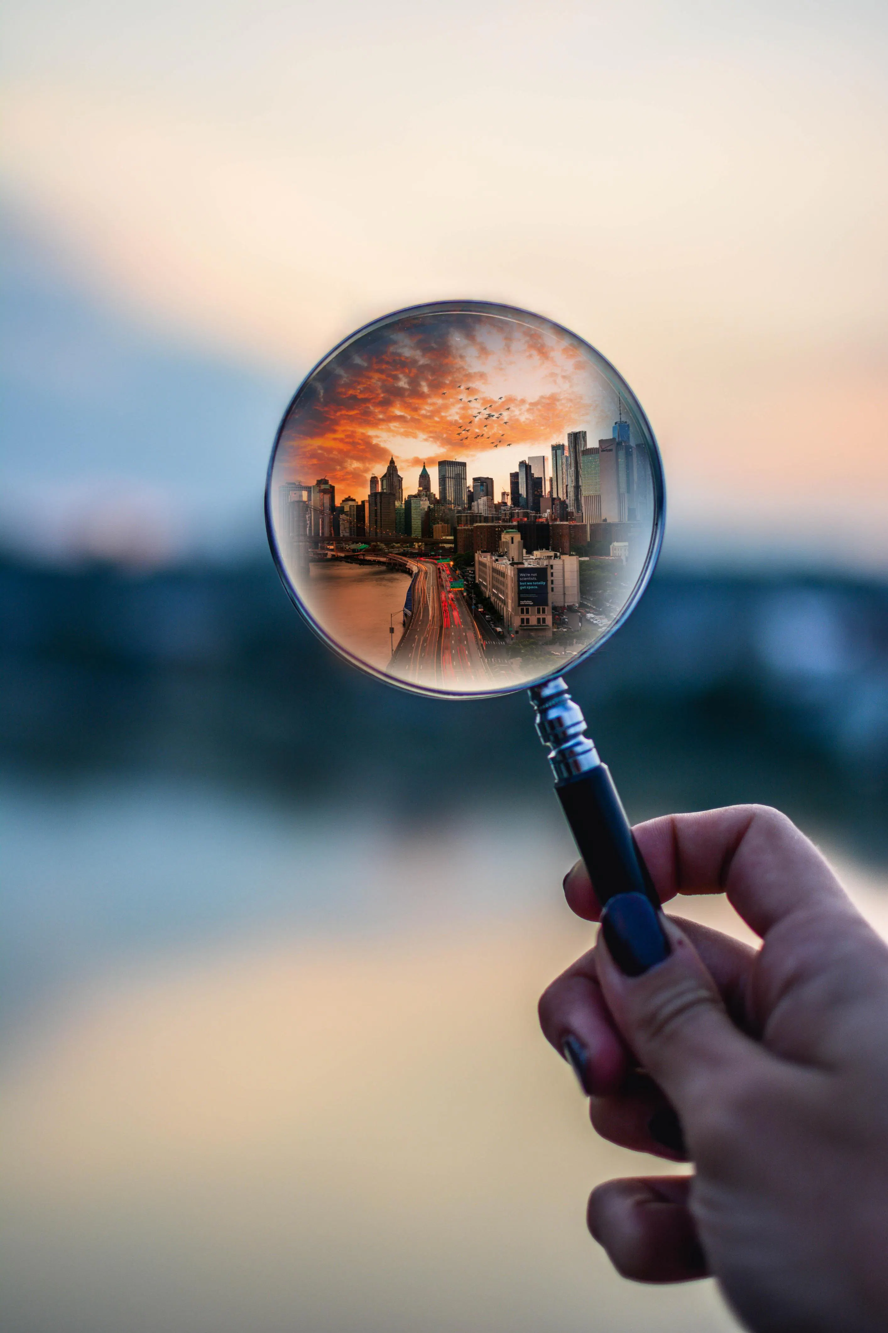 magnifying glass held by a womans hand, with the view of a bustling city in glass