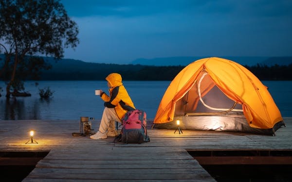 A woman camping with an orange tent and a backpack